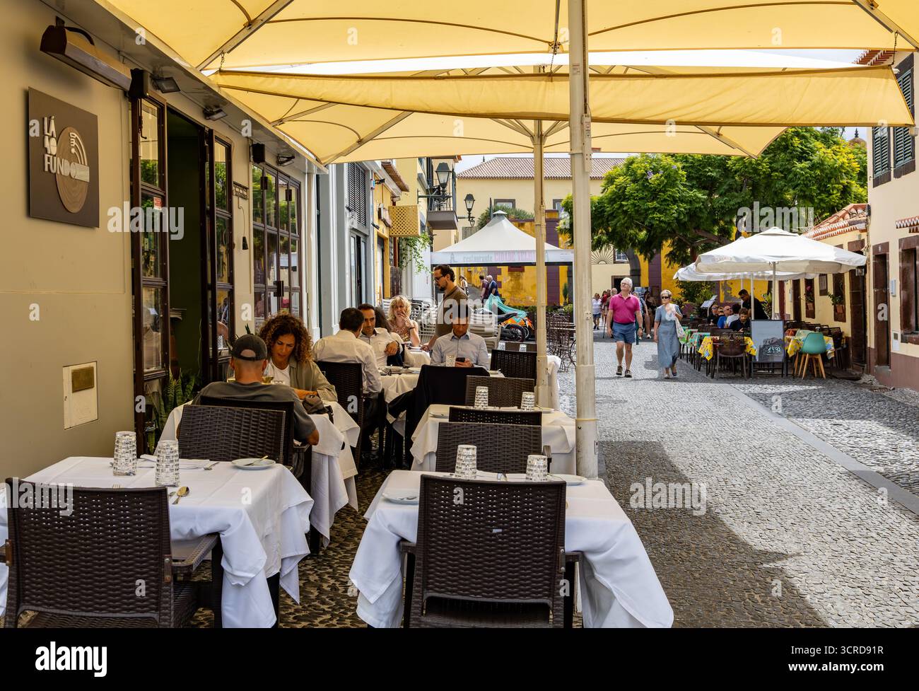 Cena all'aperto in una caffetteria europea con persone che si godono i pasti sotto grandi ombrelloni su una strada pedonale lastricata Funchal Madeira Foto Stock