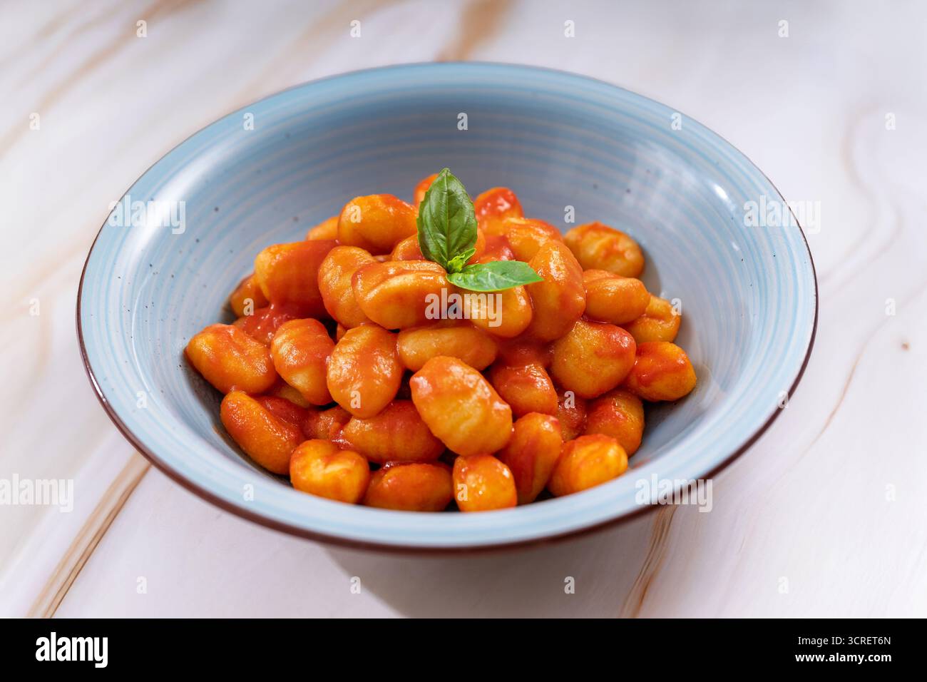 Gnocchi in una ciotola blu con salsa di pomodoro e foglia di basilico fresco Foto Stock
