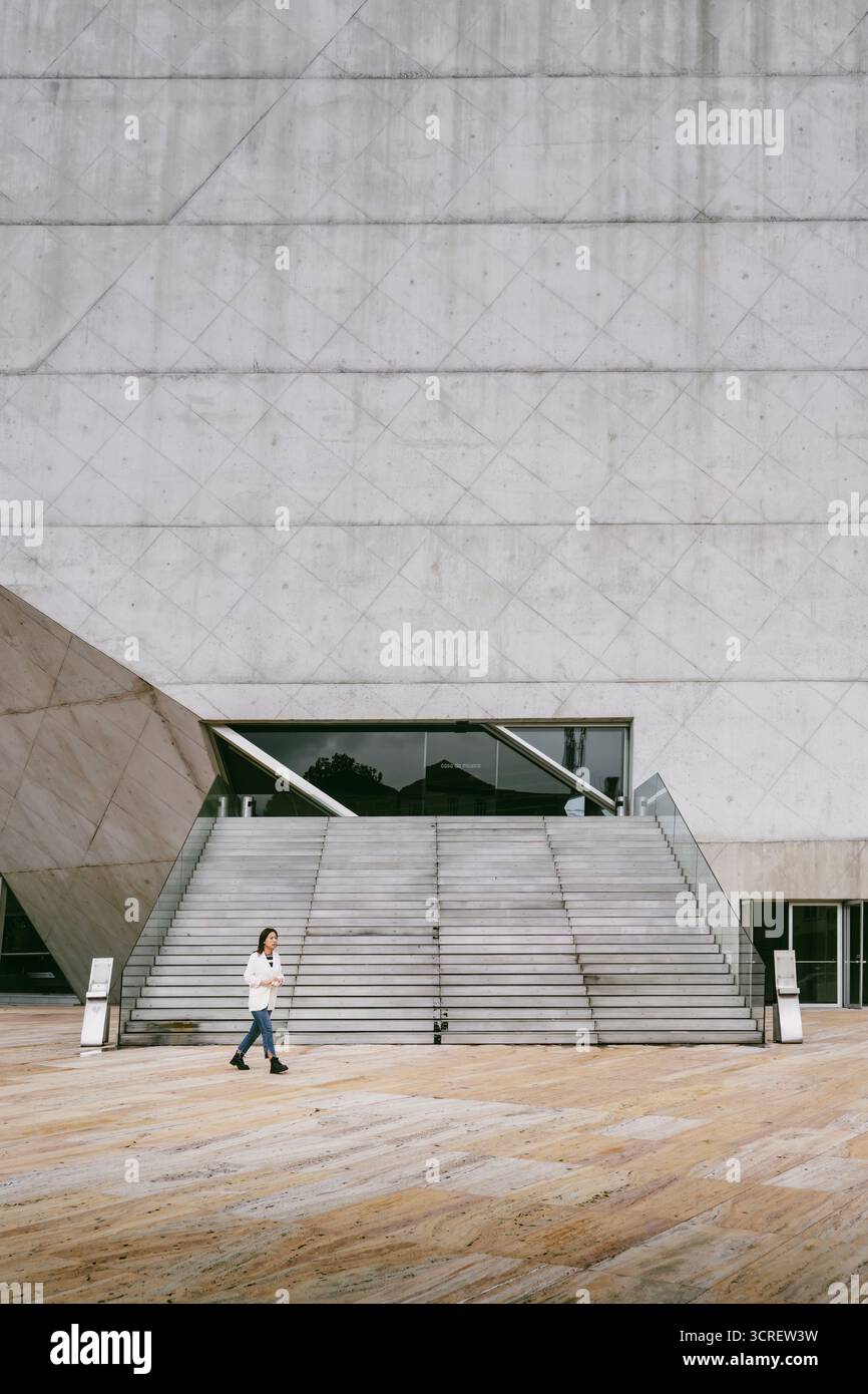 Donna che cammina attraverso la scala principale e la facciata in cemento della Casa della musica (Casa da Música), progettata da Rem Koolhaas a Porto, Portogallo Foto Stock