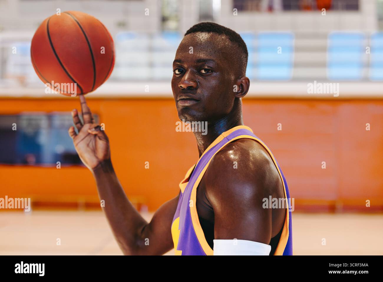 Giocatore di basket che gira senza sforzo una palla al dito, dando prova di tranquillità mentre guarda la fotocamera. Foto Stock