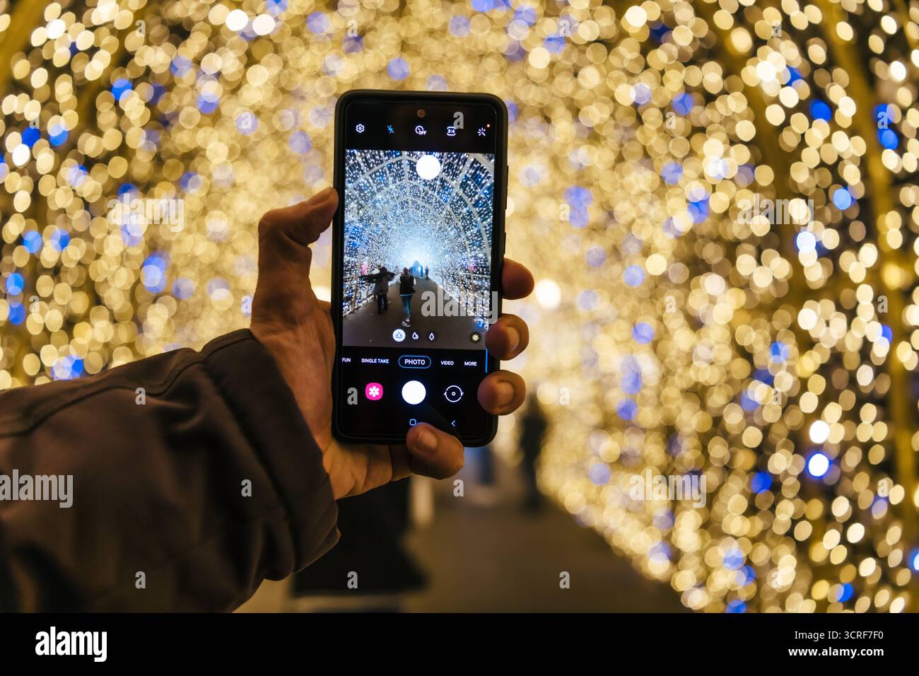 Vista di un telefono che cattura un tunnel luminoso di luci bokeh bianche e blu, creando uno spettacolo affascinante, la città di Lussemburgo, Lussemburgo. Foto Stock