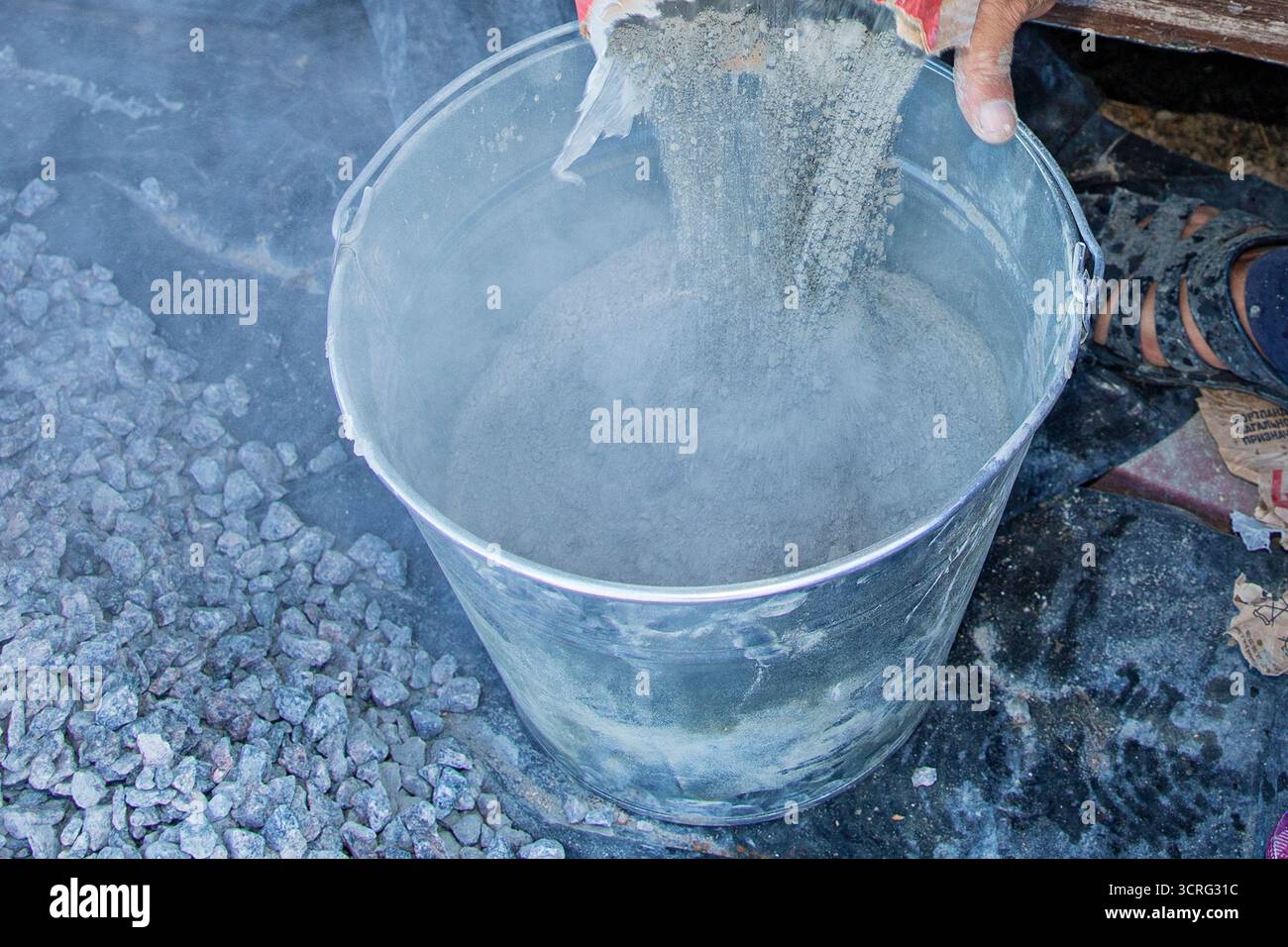 Primo piano della polvere di cemento secco versata dal sacchetto nel secchio metallico durante la costruzione. Concetto di materiali da costruzione, preparazione del calcestruzzo, muratura Foto Stock