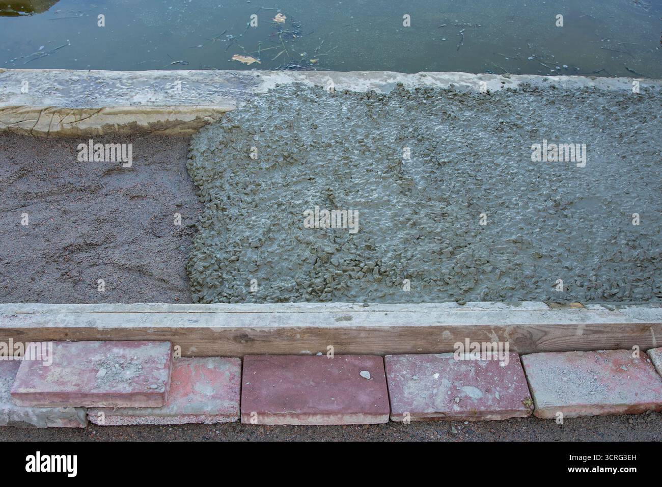 Primo piano di calcestruzzo fresco bagnato versato su una base sabbiosa vicino alla riva dell'acqua all'interno di casseri in legno. Concetto di costruzione di banchine, lavori di fondazione, lungomare Foto Stock