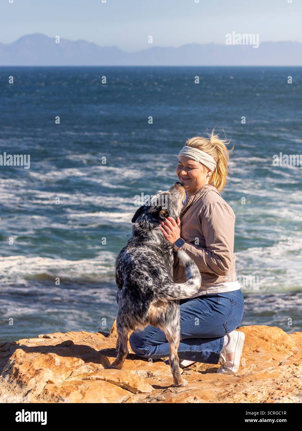 Una donna con un cane australiano (Blue Heeler) all'aperto che esplora insieme al cane che salta e la bacia Foto Stock