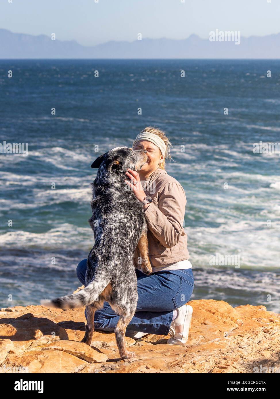 Una donna con un cane australiano (Blue Heeler) all'aperto che esplora insieme al cane che salta e la bacia Foto Stock