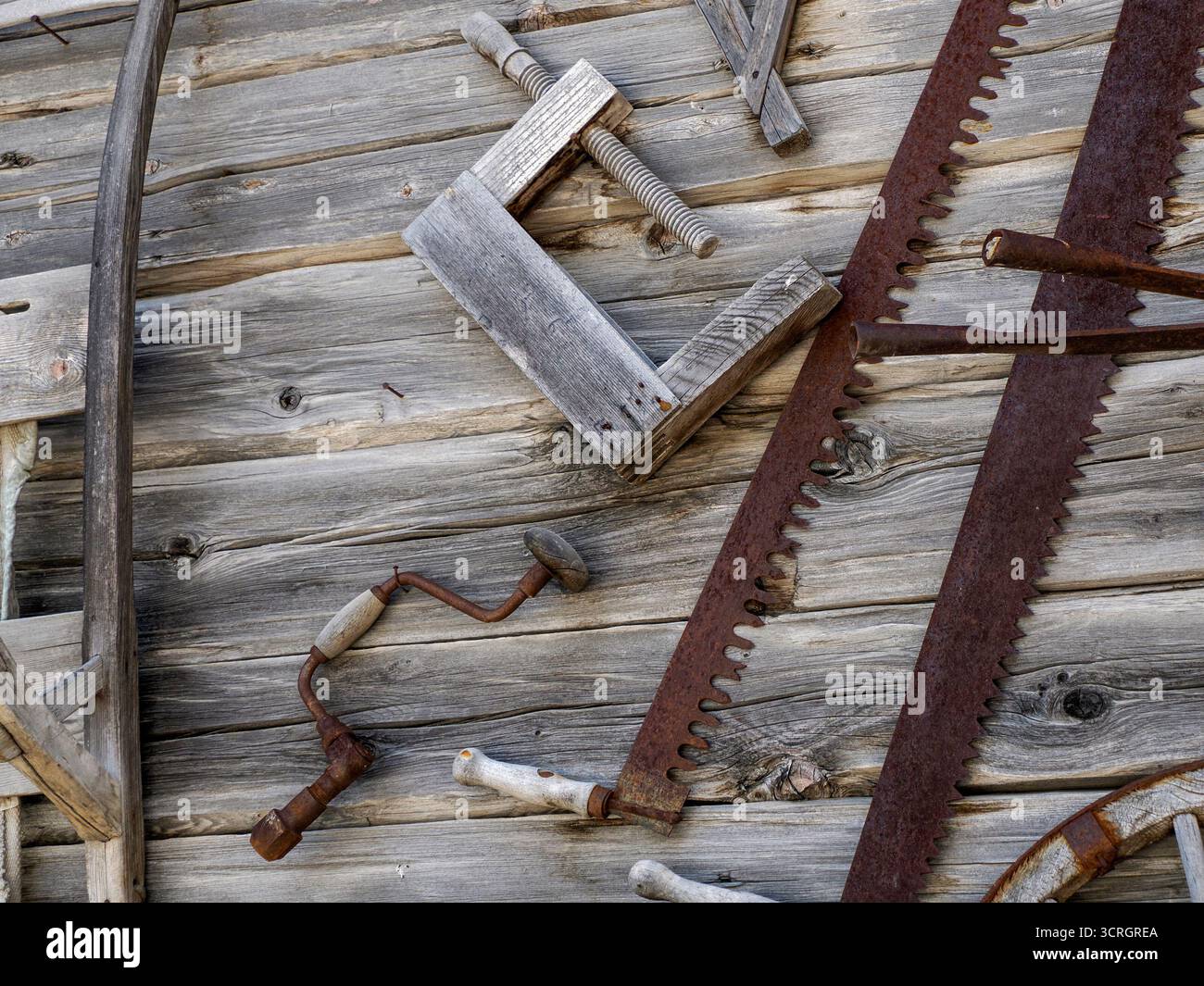 Alcuni vecchi attrezzi agricoli sulla parete della cabina di legno Foto Stock