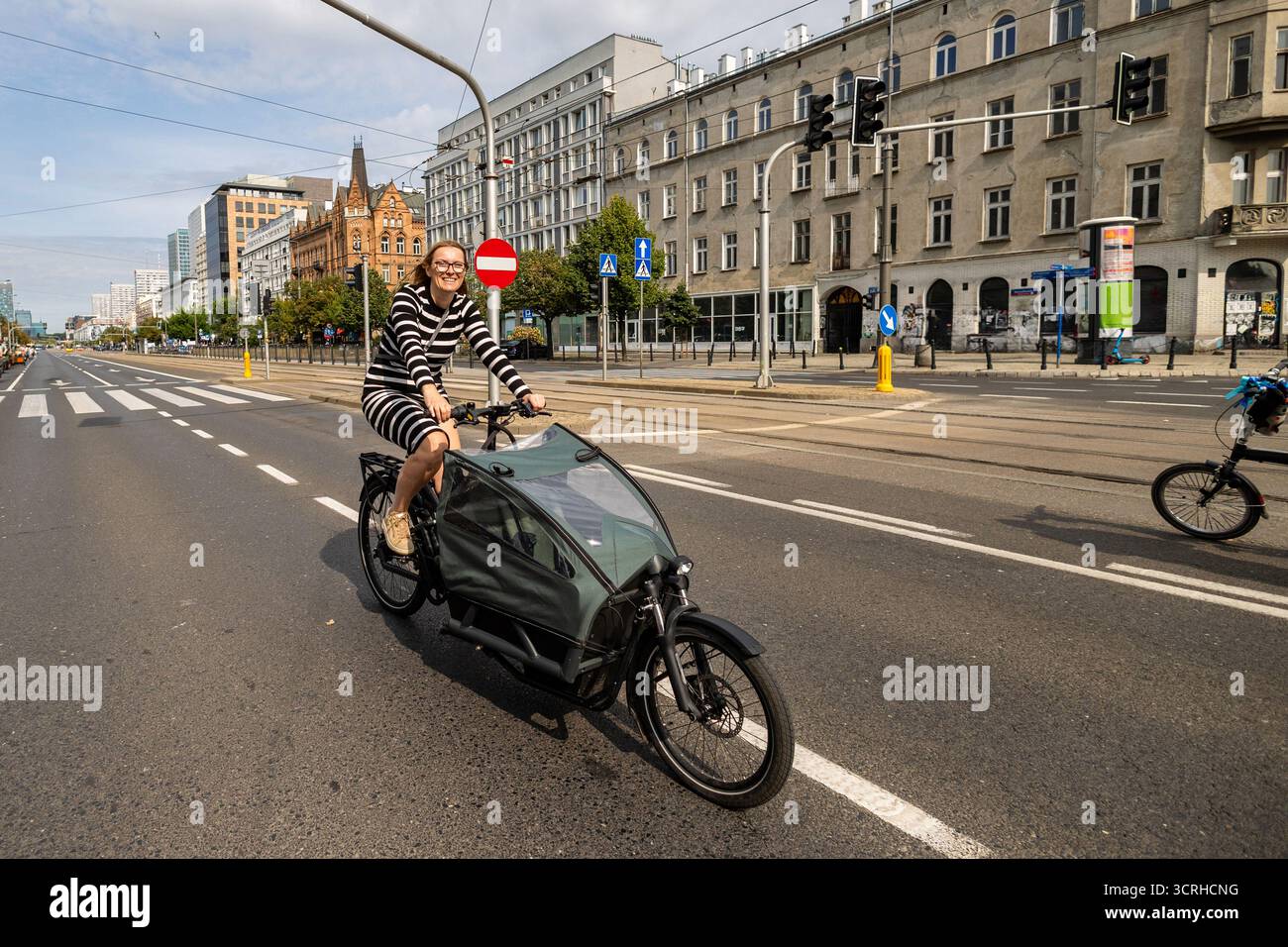 Giovane donna in sella a una bici cargo in città in una giornata di sole Foto Stock