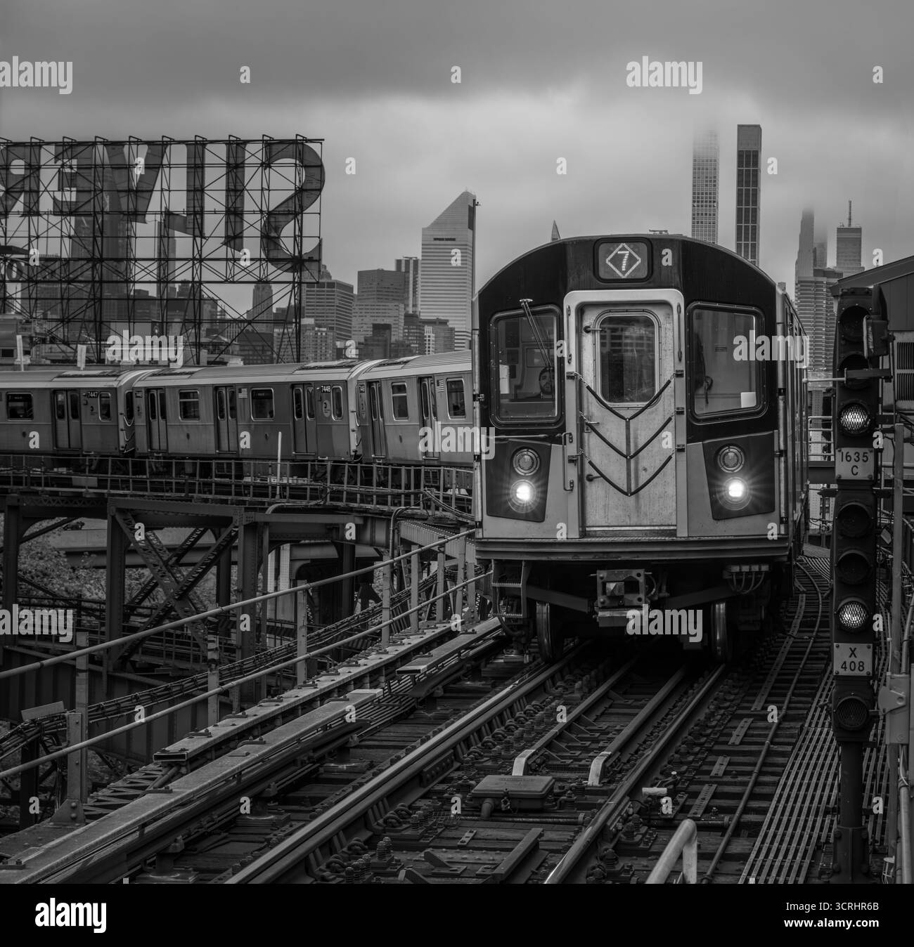 Metropolitana urbana n. 7 treno New York in arrivo su binari sopraelevati con lo skyline della città sullo sfondo - scena dei trasporti moderni in Moody Light Foto Stock