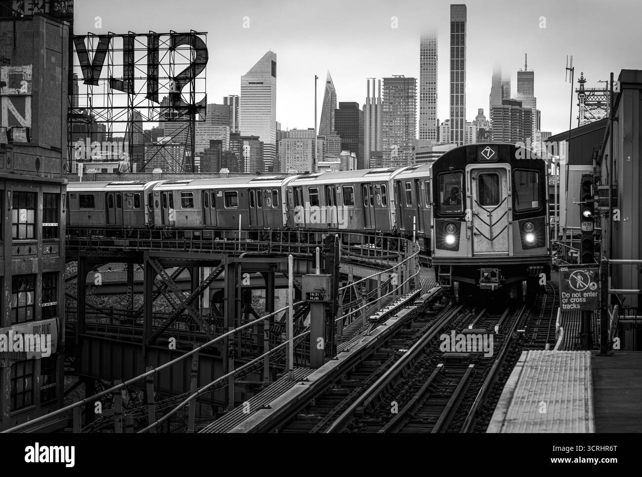 Metropolitana urbana n. 7 treno New York in arrivo su binari sopraelevati con lo skyline della città sullo sfondo - scena dei trasporti moderni in Moody Light Foto Stock