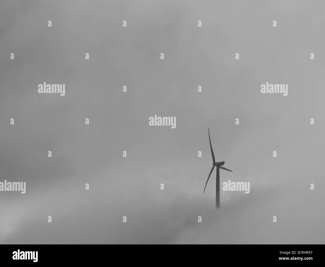 Turbine eoliche che emergono da nuvole nebbiose – scenario minimalista di energia rinnovabile che simboleggia la sostenibilità e l'energia pulita Foto Stock