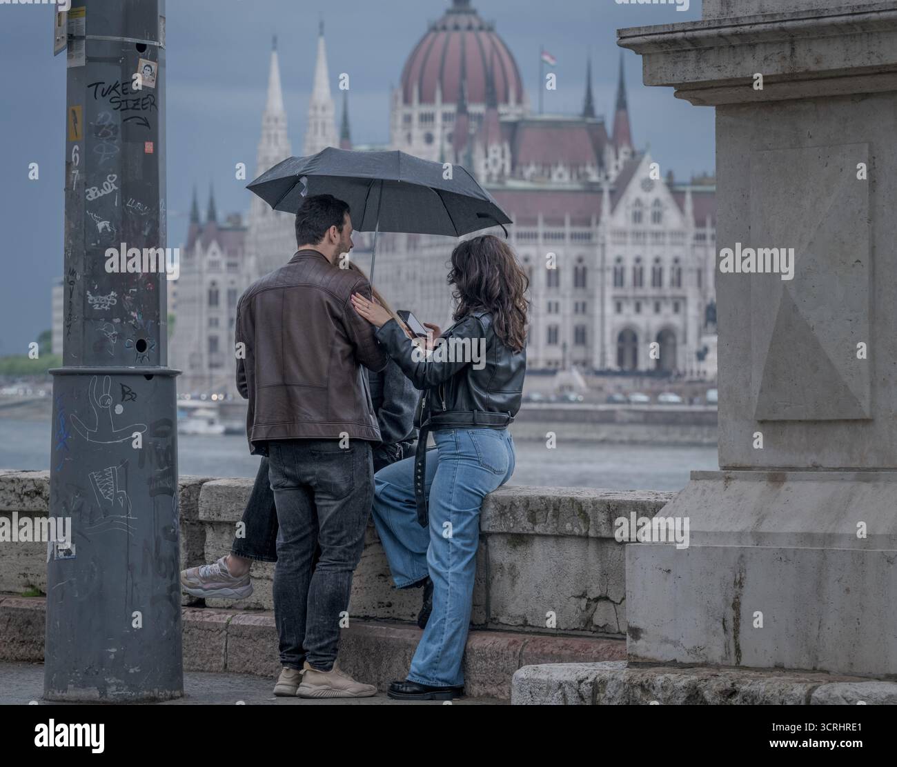 Coppia in piedi sotto l'ombrello il giorno della pioggia con vista sull'edificio storico - momento romantico di strada nella città europea Foto Stock