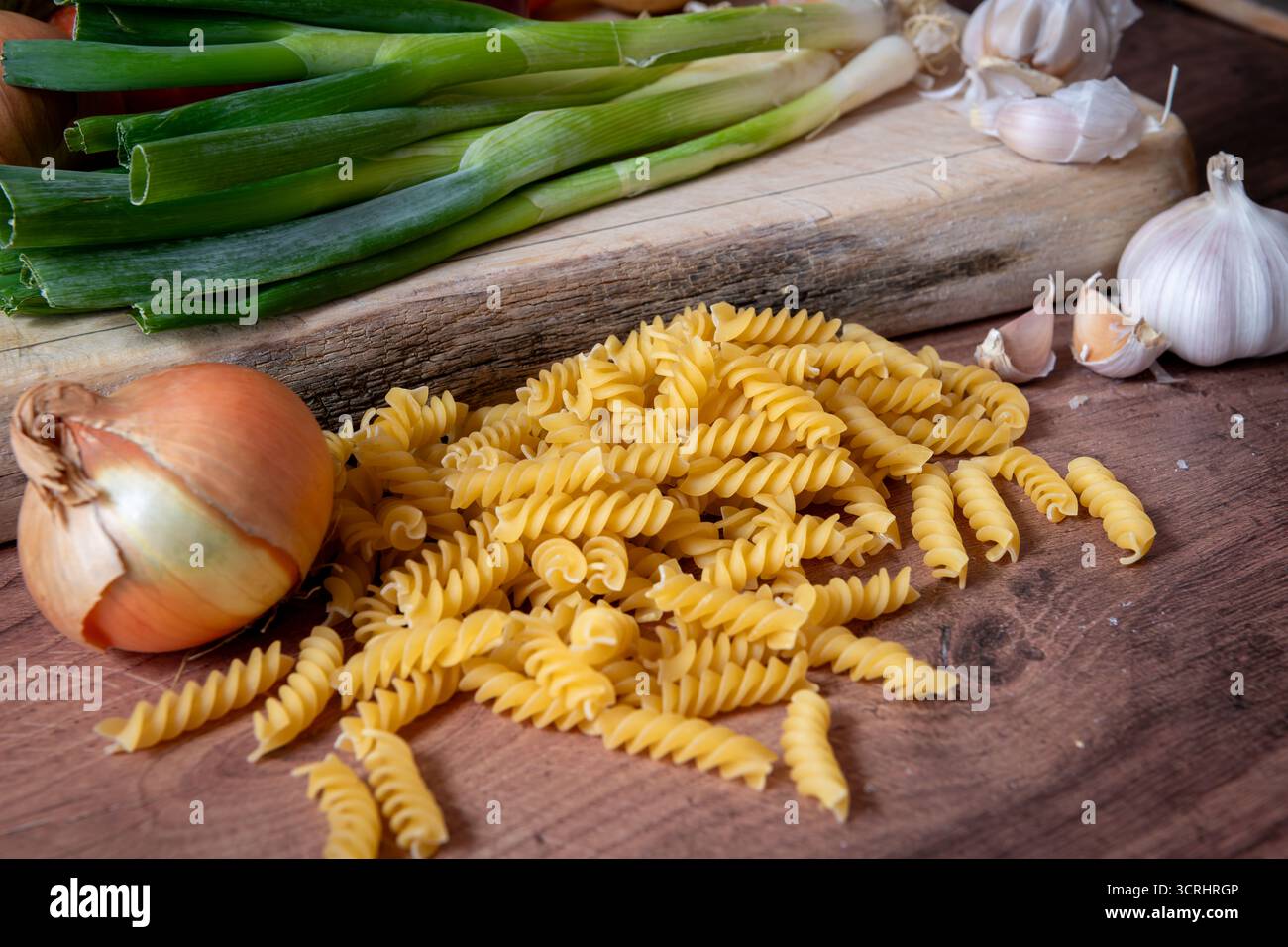 Un mucchio di pasta italiana secca Fusilli su un piano di lavoro della cucina insieme a varie verdure. Foto Stock