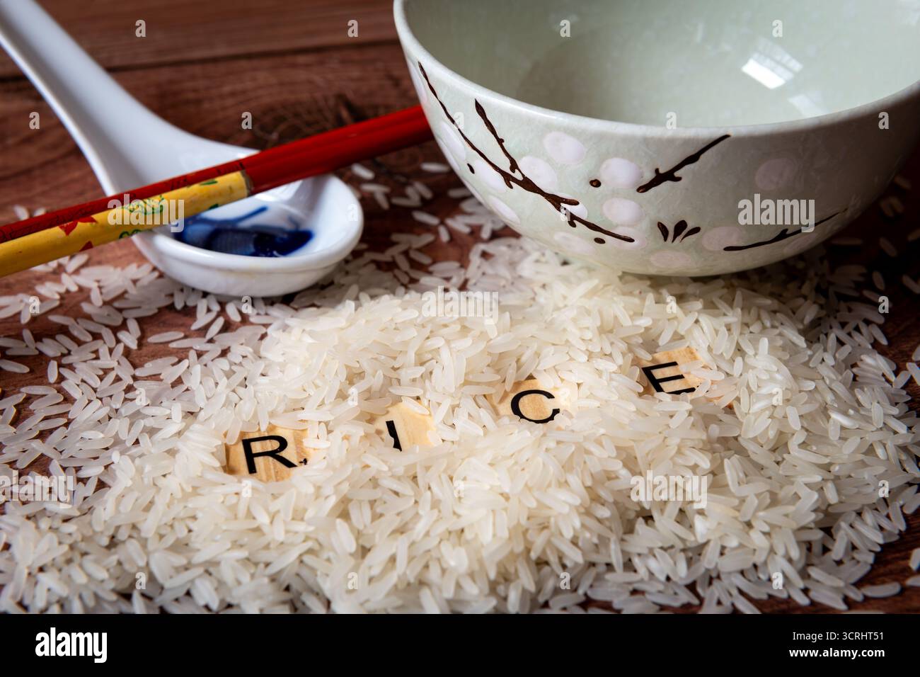 Un mucchio di riso bianco su un piano di lavoro della cucina insieme a un cucchiaio di ceramica, un recipiente e un paio di bacchette. Foto Stock