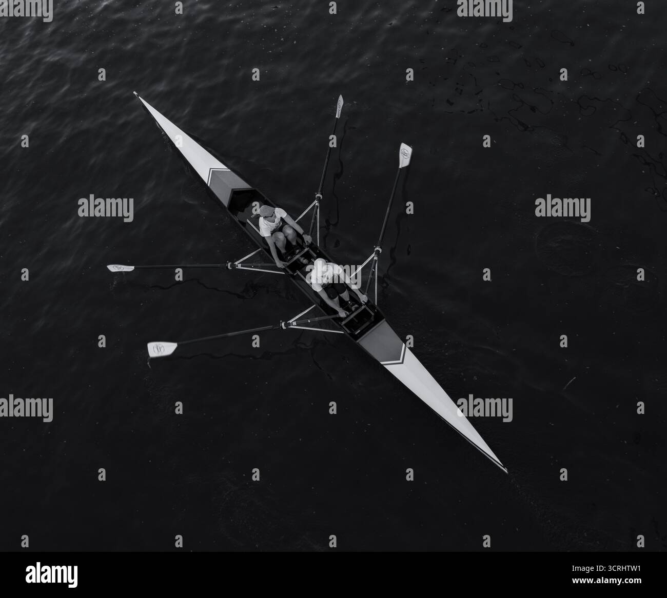 Vista aerea di due razze in barca da corsa sull'acqua calma, lavoro di squadra e precisione in movimento catturati in bianco e nero minimalista Foto Stock