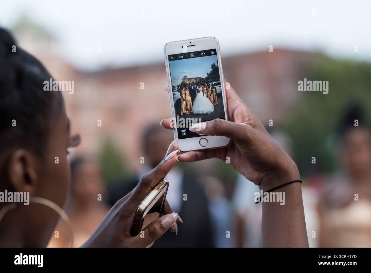 Donna che scatta una foto di matrimonio con uno smartphone, catturando un momento di celebrazione moderna in un ambiente urbano all'aperto Foto Stock