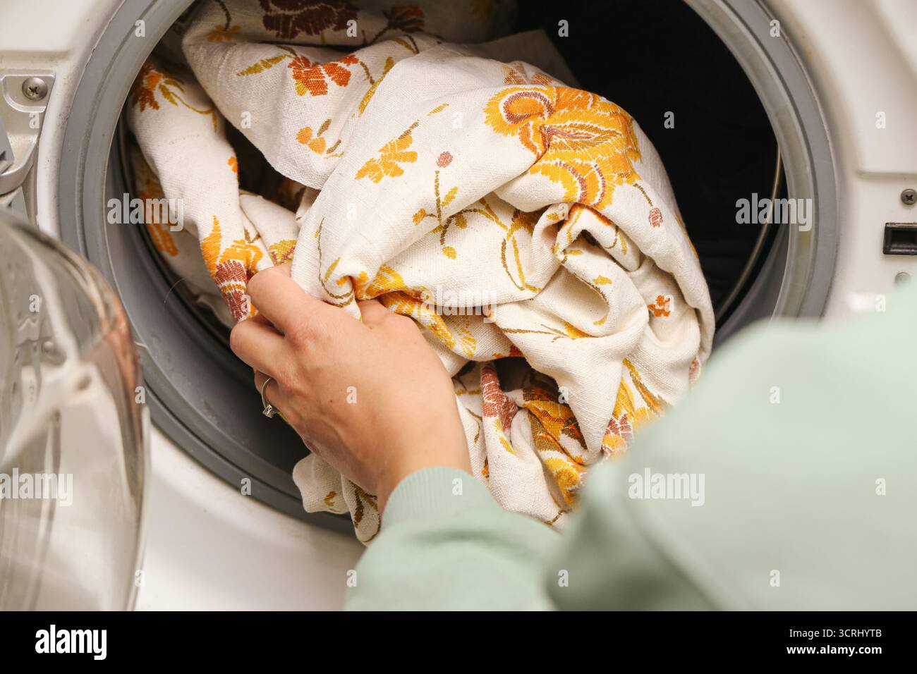 Donna che carica il tessuto decorativo in lino beige nella lavatrice del carico frontale. Lavanderia in tessuto naturale. Pulizia della casa e pulizia dei tessuti Foto Stock