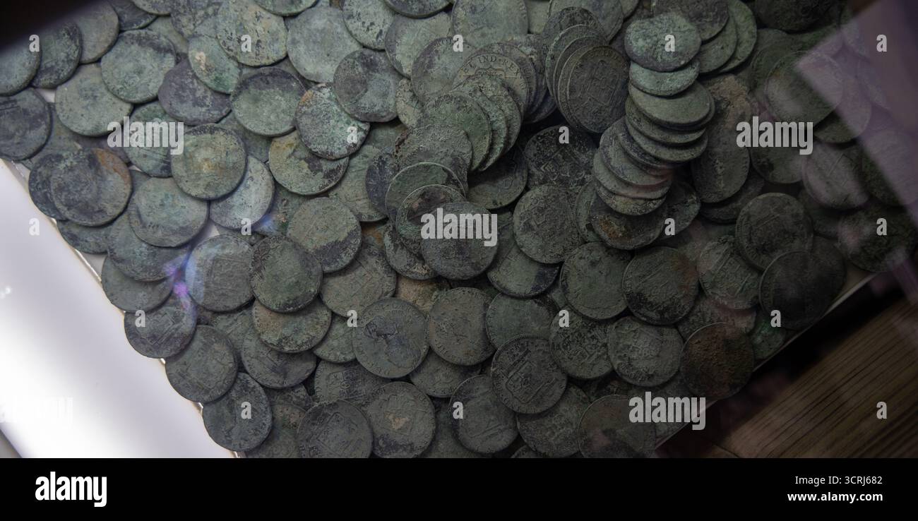 Una grande collezione di monete antiche esposte sotto vetro, mostrando le loro superfici usurate e intemperie, con alcune monete impilate e altre sparse Foto Stock