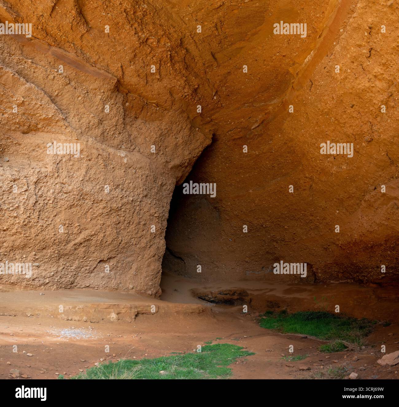 Un ingresso naturale nella grotta con formazioni rocciose rossastre e erba verde alla base. Foto Stock