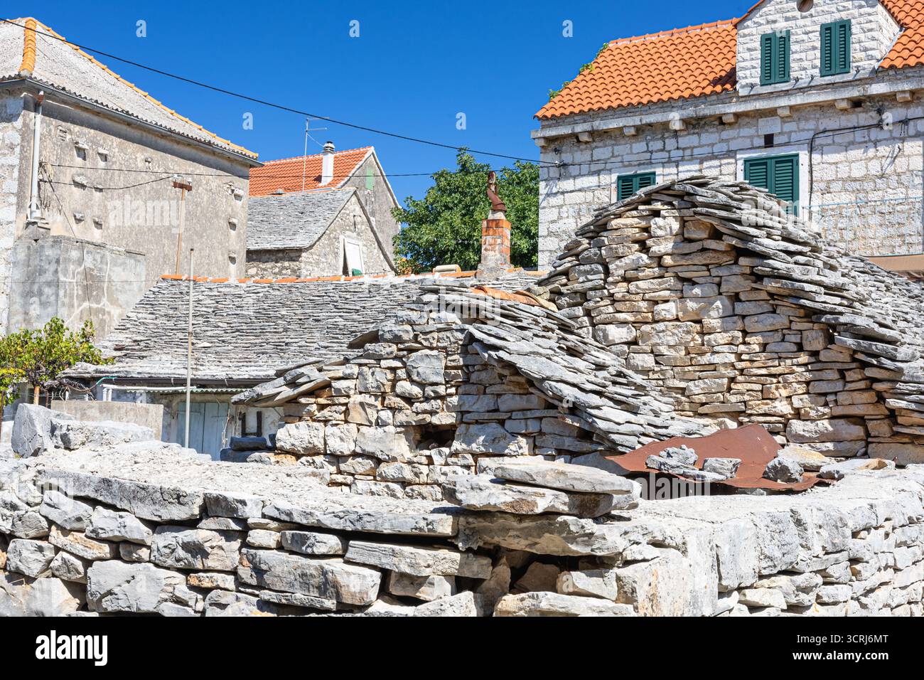 Un villaggio illuminato dal sole caratterizzato da case in pietra intemprata, muretti a secco sovrapposti e tetti di tegole rosse, che trasmettono fascino rustico e architettura tradizionale Foto Stock