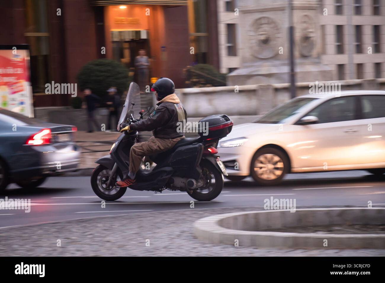 Belgrado, Serbia - 1° ottobre 2025: Motociclista in sella a uno scooter nella trafficata strada della città la sera Foto Stock