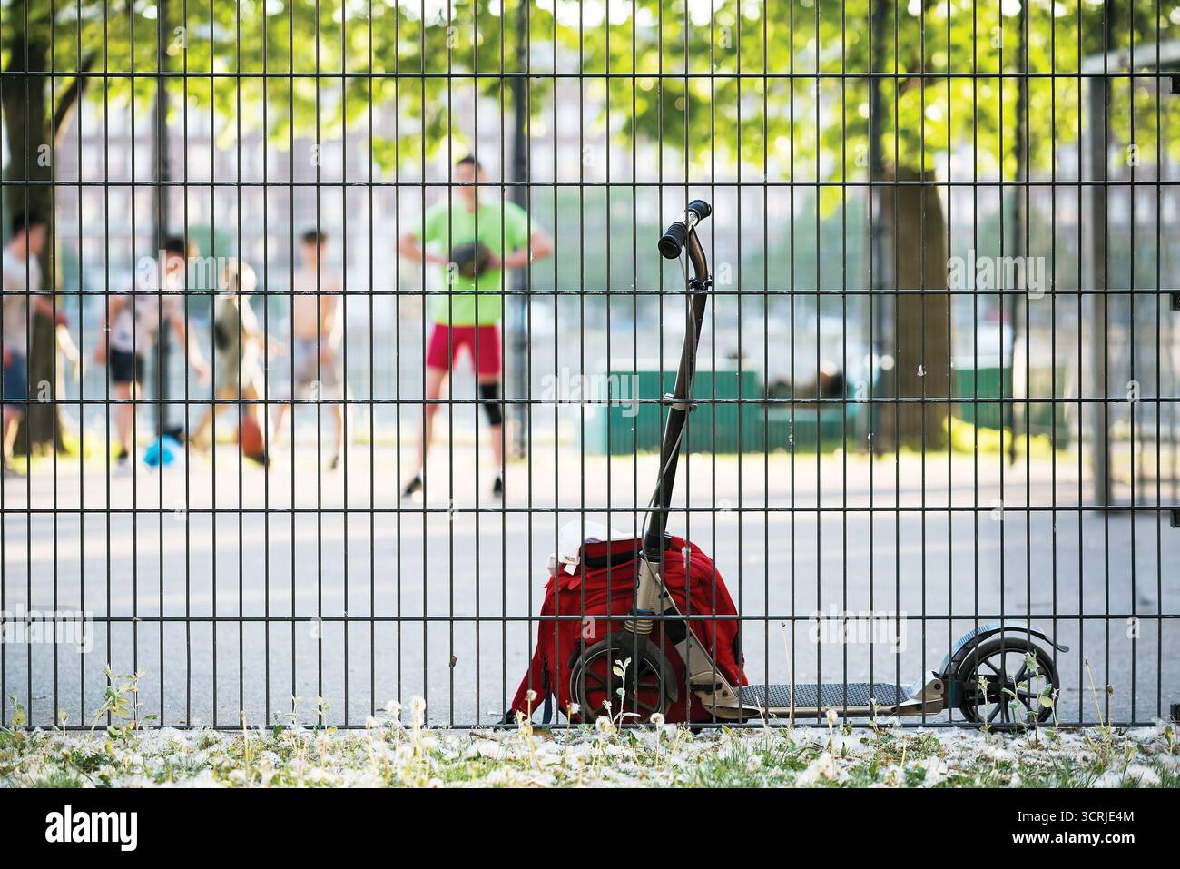 Scooter e zaino in prossimità di una recinzione sportiva contro una persona sfocata che gioca a basket Foto Stock