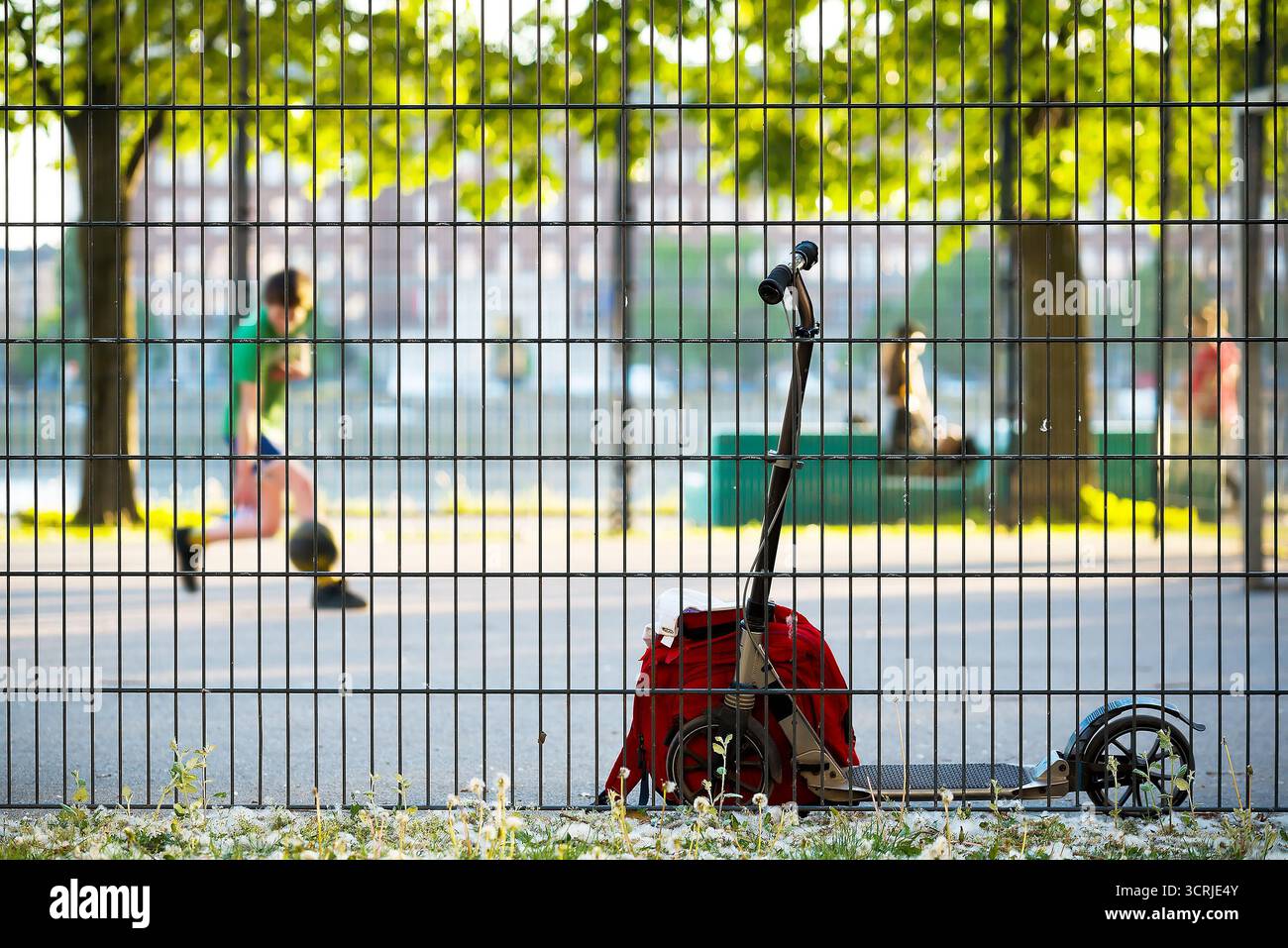 Scooter e zaino in prossimità di una recinzione sportiva contro bambini deconcentrati che giocano a basket Foto Stock