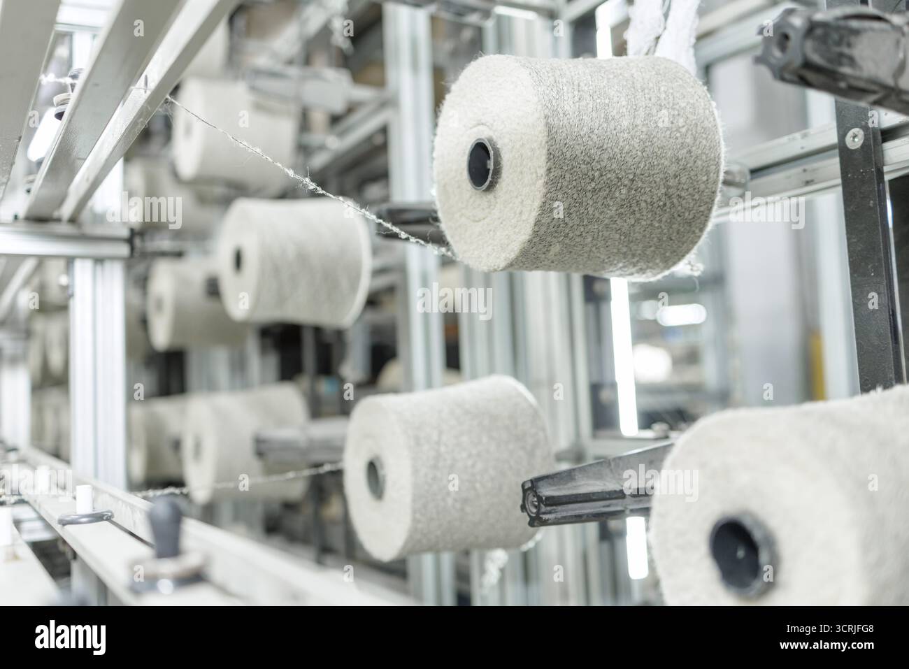 Coni di filati su filati di creme che alimentano le attrezzature per la filatura in una moderna fabbrica tessile per l'industria e i temi di produzione Foto Stock