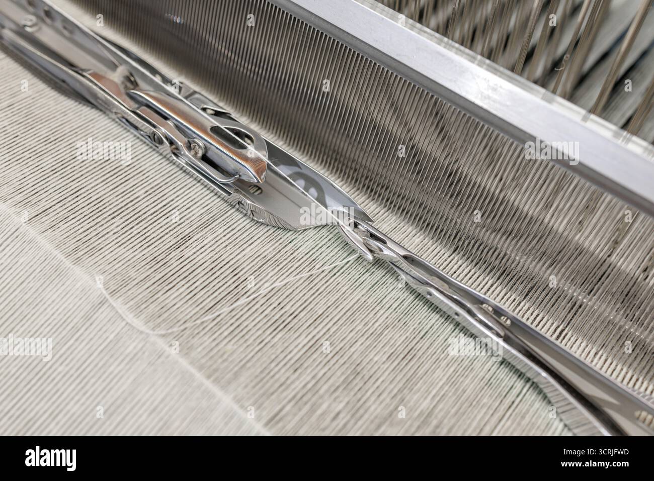Vista ravvicinata della navetta che si muove lungo le canne su un moderno telaio con ordito e trama in una fabbrica tessile che mostra tessitura di precisione e produzione di qualità Foto Stock