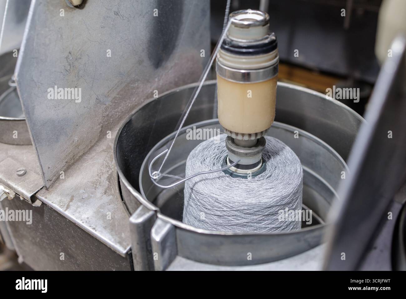 Il cono del filato scorre attraverso un alimentatore di tensione su una bobinatrice in una fabbrica tessile che mostra la preparazione per la lavorazione a maglia o la tessitura Foto Stock