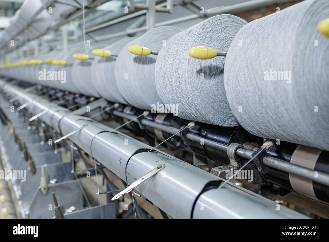 I grandi rotoli di filati alimentano una linea di deformatura in una fabbrica tessile che mostra un flusso di lavoro di precisione per l'automazione e una produzione di qualità Foto Stock