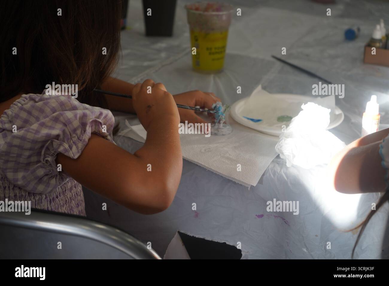 Un bambino con i capelli castani, visto da dietro, è concentrato su un'attività artistica, tenendo in mano un pennello per dipingere una miniatura. Foto Stock