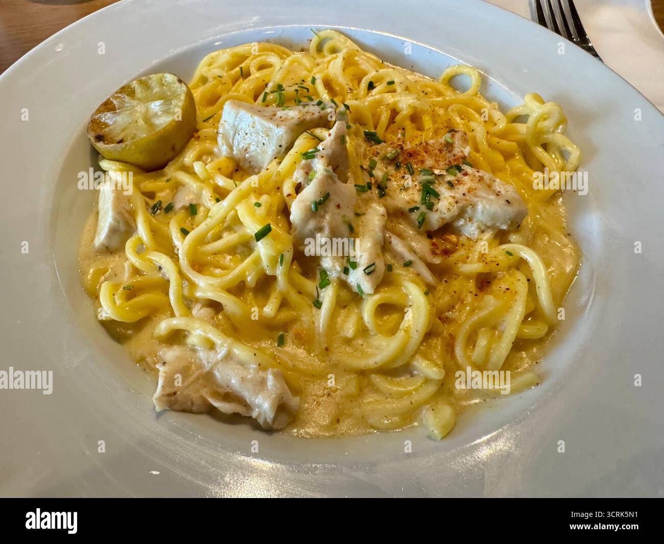 Un piatto di tagliatelle cremose condite con formaggio grattugiato ed erbe aromatiche, presentato su un tavolo rustico. Foto Stock