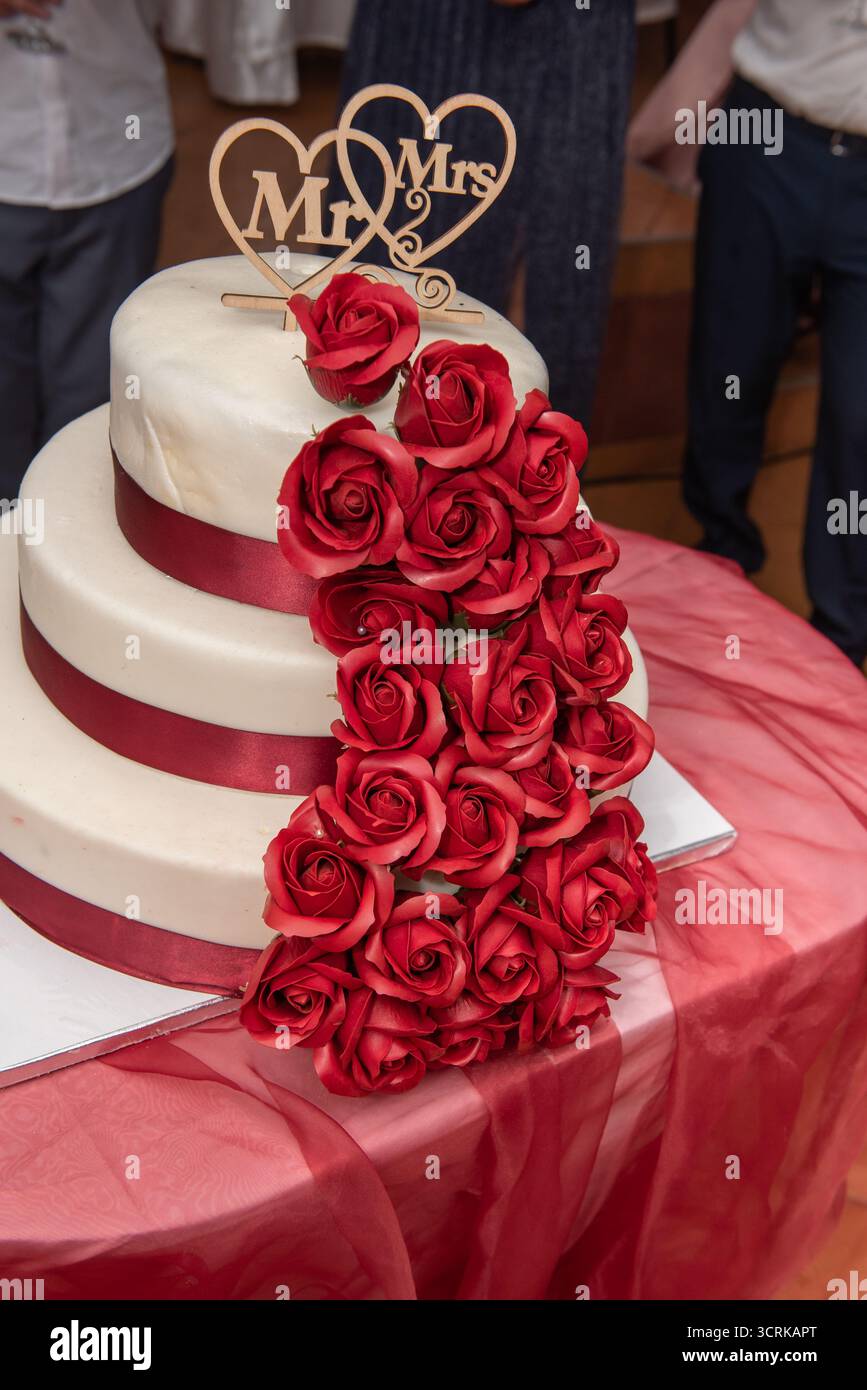 Torta nuziale a tre piani decorata con rose rosse e glassa bianca, Foto Stock
