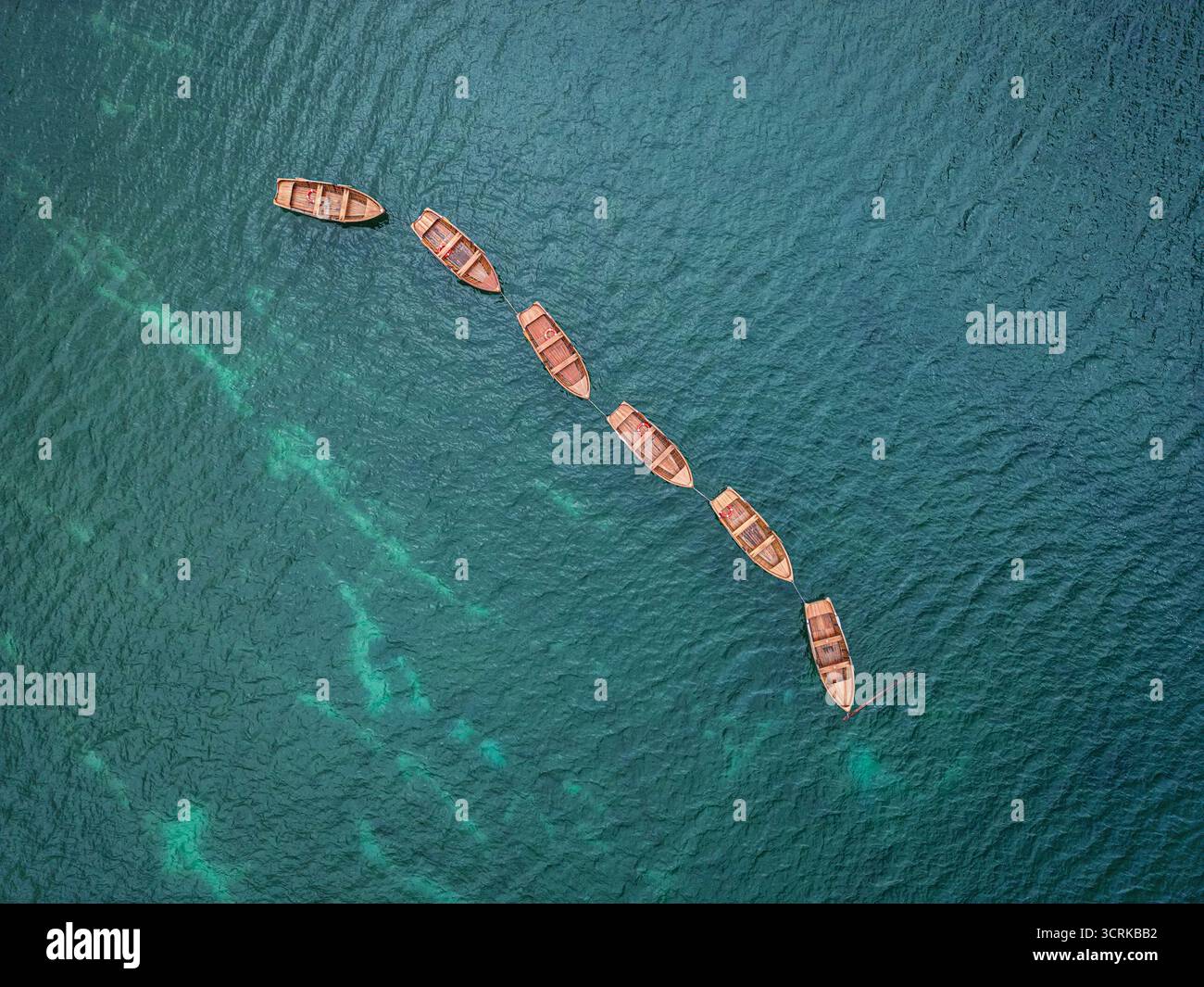 Vista aerea idilliaca e tranquilla di alcune barche a remi in fila su un lago turchese o sull'acqua di mare. Acqua tranquilla e attività ricreative. Dolomiti, Italia Foto Stock