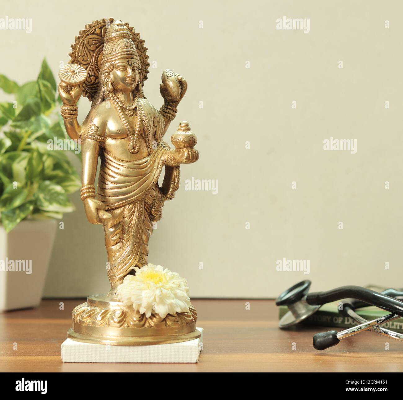Statua in ottone di Lord Dhanvantari con fiori di calendula e stetoscopio su sfondo bianco. Foto Stock