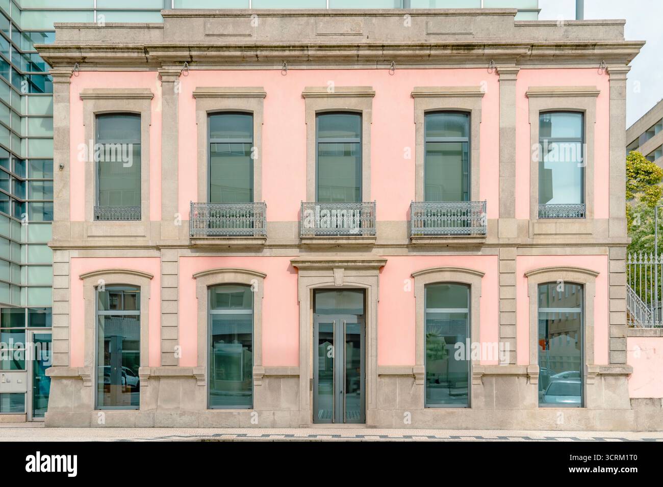 Edificio storico rosa simmetrico con finiture in pietra e balconi in ferro battuto contrastanti con moderne facciate in vetro nel centro della città Foto Stock