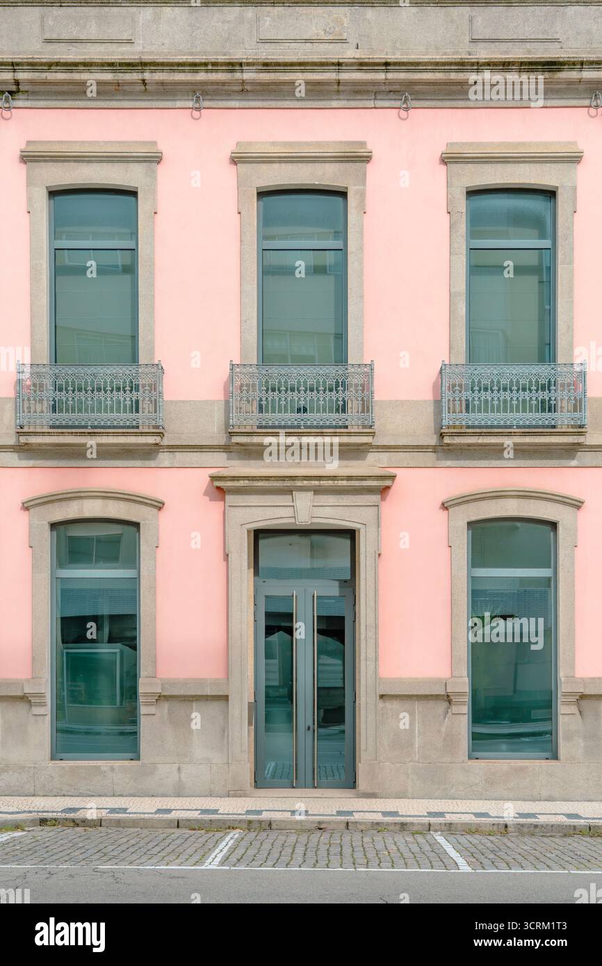 Facciata simmetrica di un edificio storico con esterno color pastello rosa, cornici in pietra e balconi in ferro battuto nel centro urbano Foto Stock