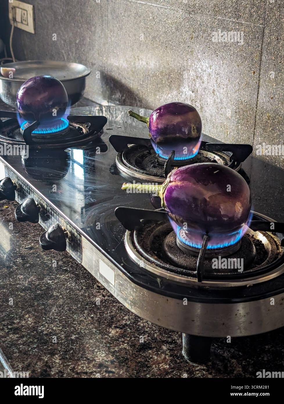 Tre melanzane viola arrostite su una stufa a gas con fiamme blu. Foto Stock
