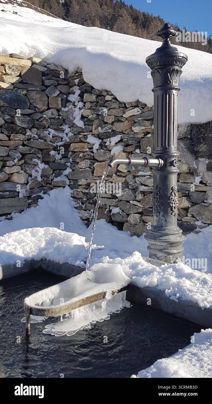 Fontana del villaggio in un villaggio dell'Engadina in inverno con neve e un muro di pietra innevato in Svizzera Foto Stock