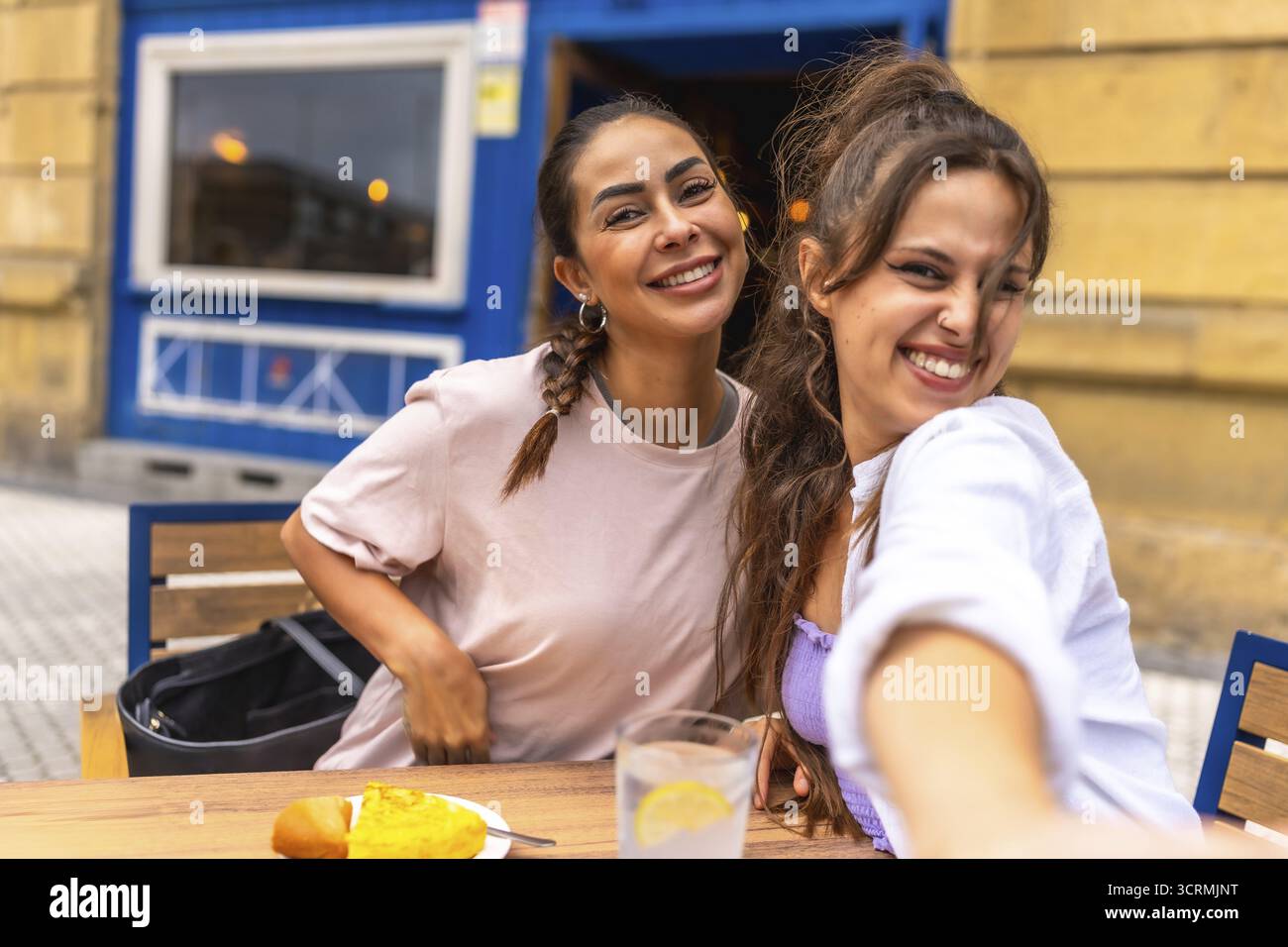 Due amici si stanno facendo un selfie mentre si gusta la colazione in un bar all'aperto, catturando un momento di gioia e di amicizia durante la loro avventura di viaggio Foto Stock