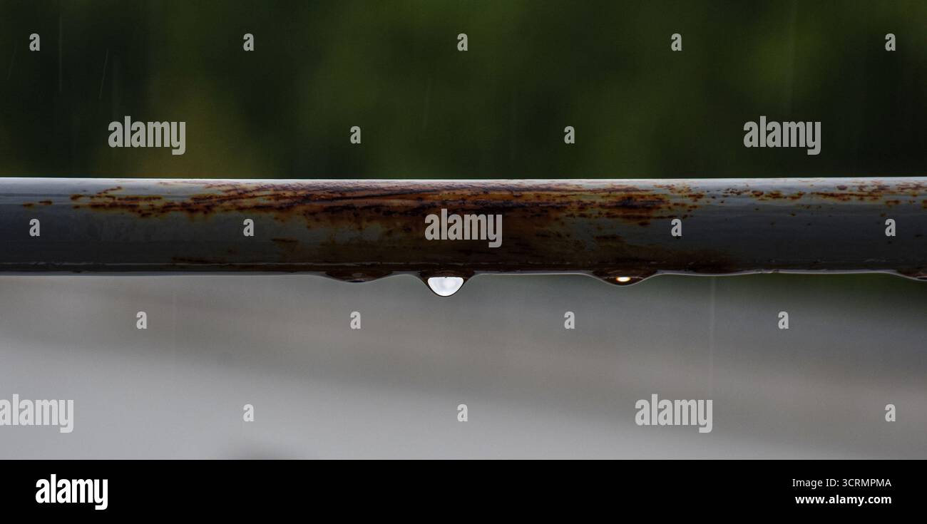 Vista dettagliata delle gocce di pioggia su una barra metallica grigia resistente agli agenti atmosferici, ringhiera della terrazza, con uno sfondo delicatamente sfocato. Foto Stock