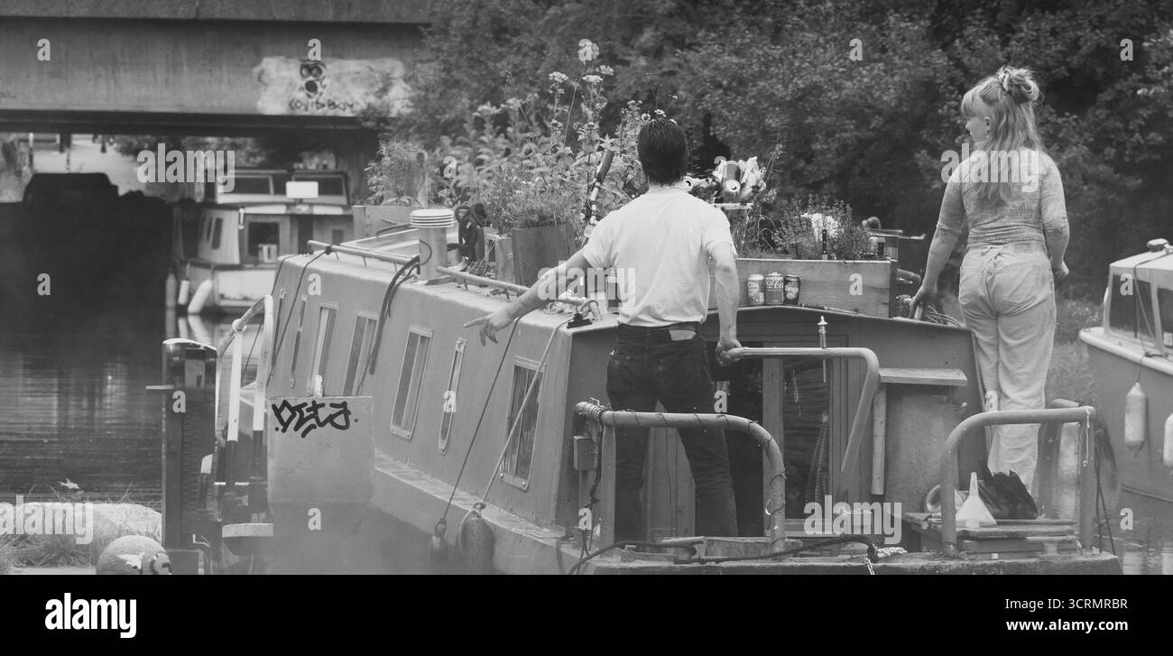 Giovane coppia su una chiatta sul canale nella città di Londra, passando attraverso una chiusa e sotto il ponte Black & White Foto Stock