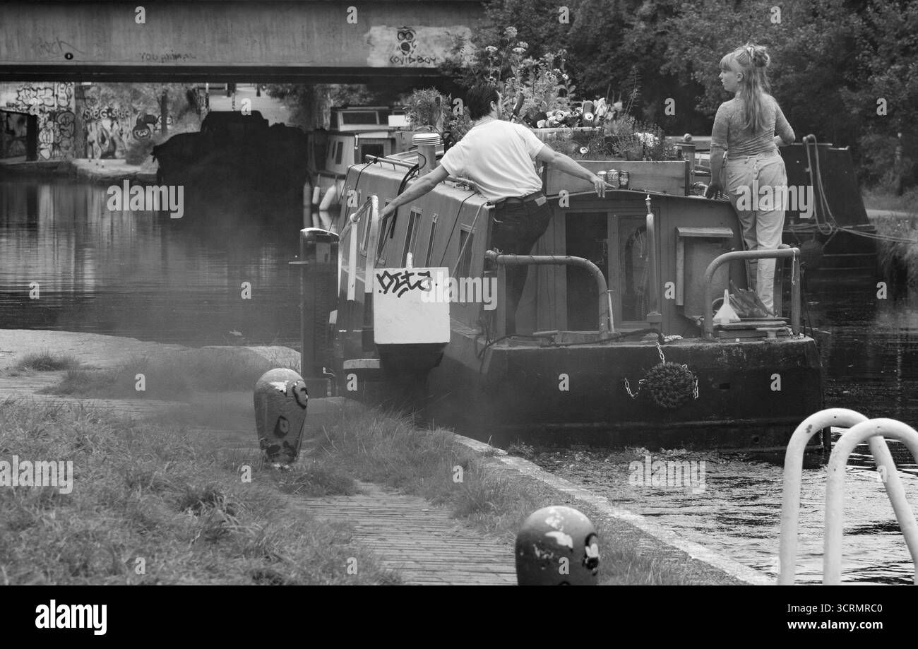 Giovane coppia su una chiatta sul canale nella città di Londra, passando attraverso una chiusa e sotto il ponte Black & White Foto Stock