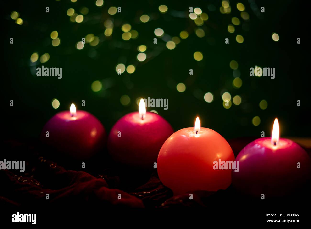 Quattro candele ardenti dell'Avvento, che simboleggiano l'amore, la pace, la gioia e la speranza, su uno sfondo verde con luci bokeh morbide Foto Stock