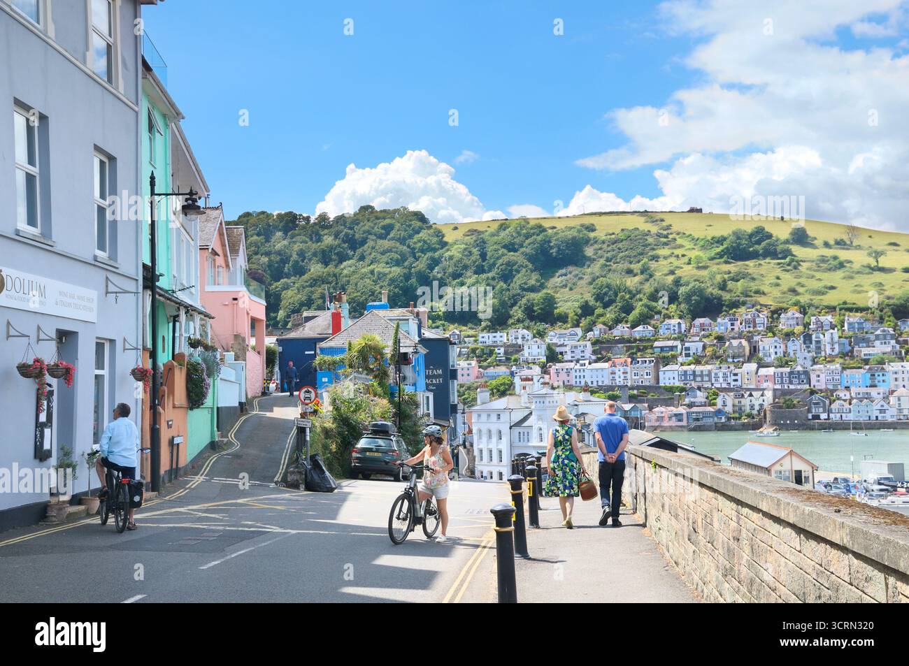 Persone che esplorano il villaggio di Kingswear in estate con una vista sul fiume Dart verso le colorate case sulle colline di Dartmouth, Devon, Inghilterra, Regno Unito Foto Stock