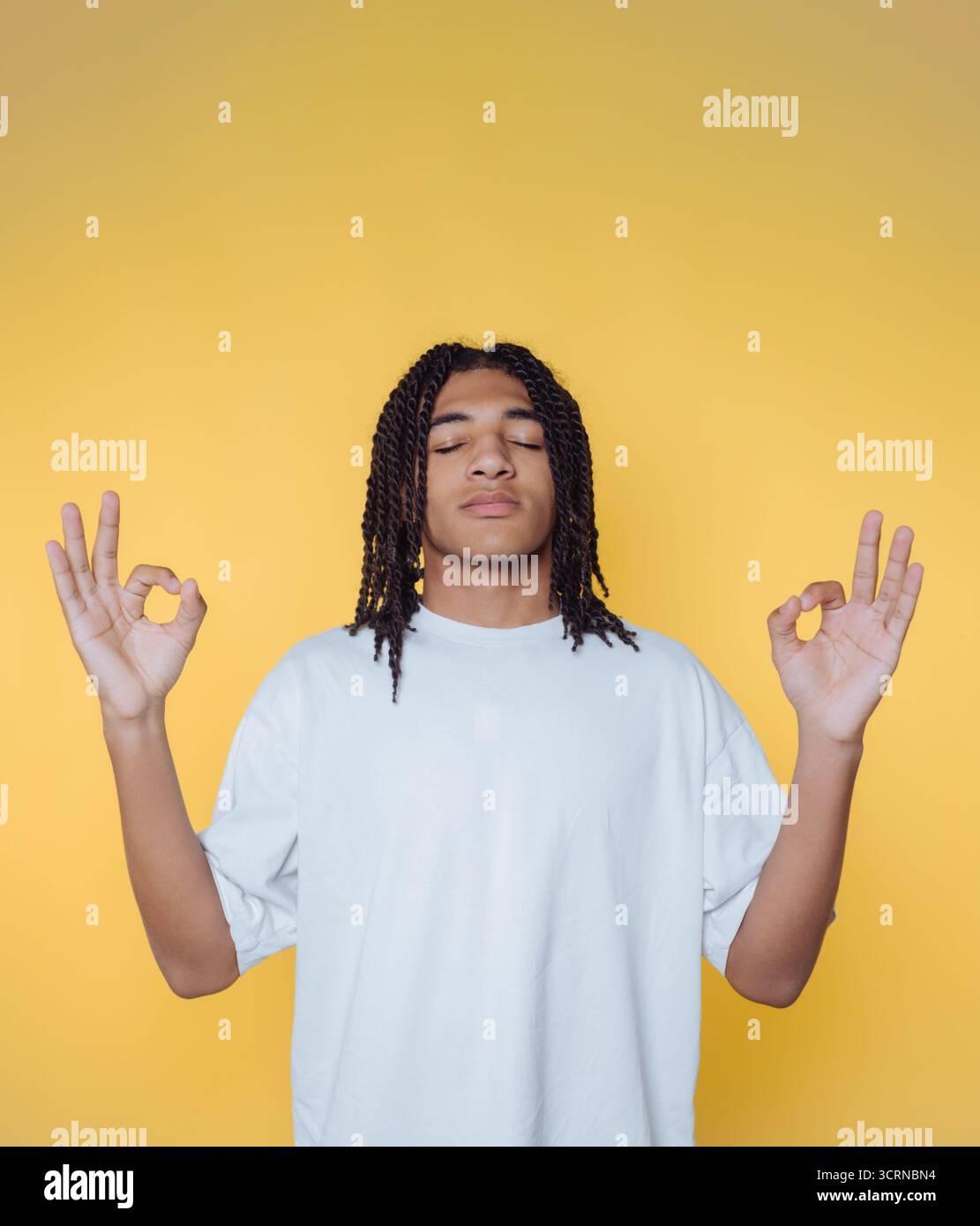 ritratto di un giovane medita pacificamente con un'aura di tranquillità, mostrando la calma interiore su sfondo giallo Foto Stock