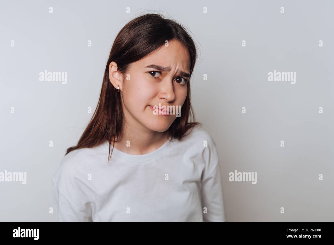Una giovane donna con lunghi capelli marroni che indossa una camicia bianca, esprimendo scetticismo. Foto Stock