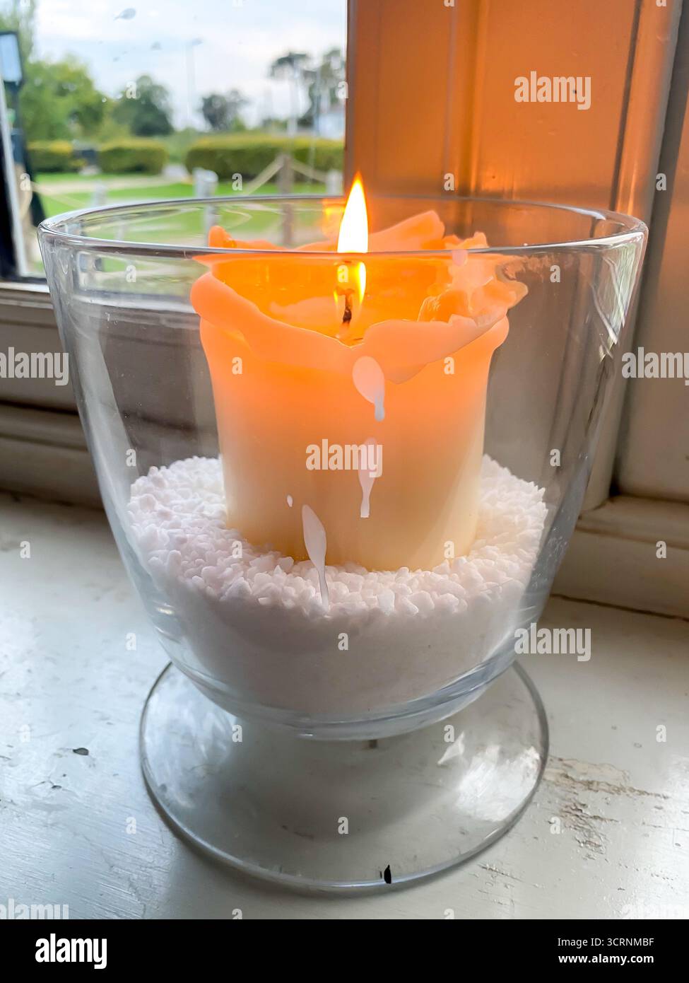 Una candela accesa in un vaso di vetro su un davanzale è un oggetto decorativo e un punto focale. Foto Stock