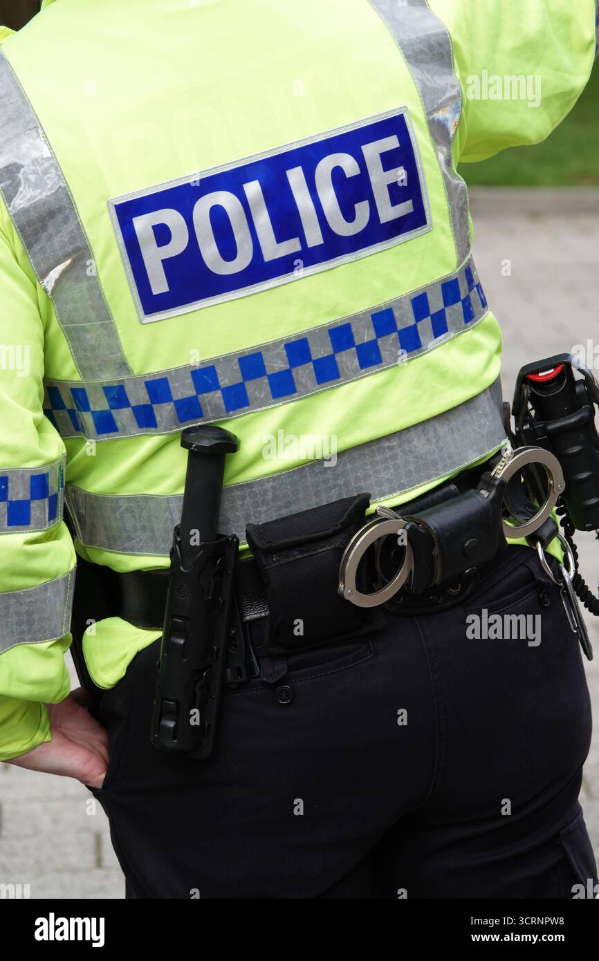 Primo piano della giacca ad alta visibilità di un agente di polizia britannico non identificabile con il testo "POLIZIA", che mostra la cintura di sicurezza munita di manette, bastone, ecc. Foto Stock