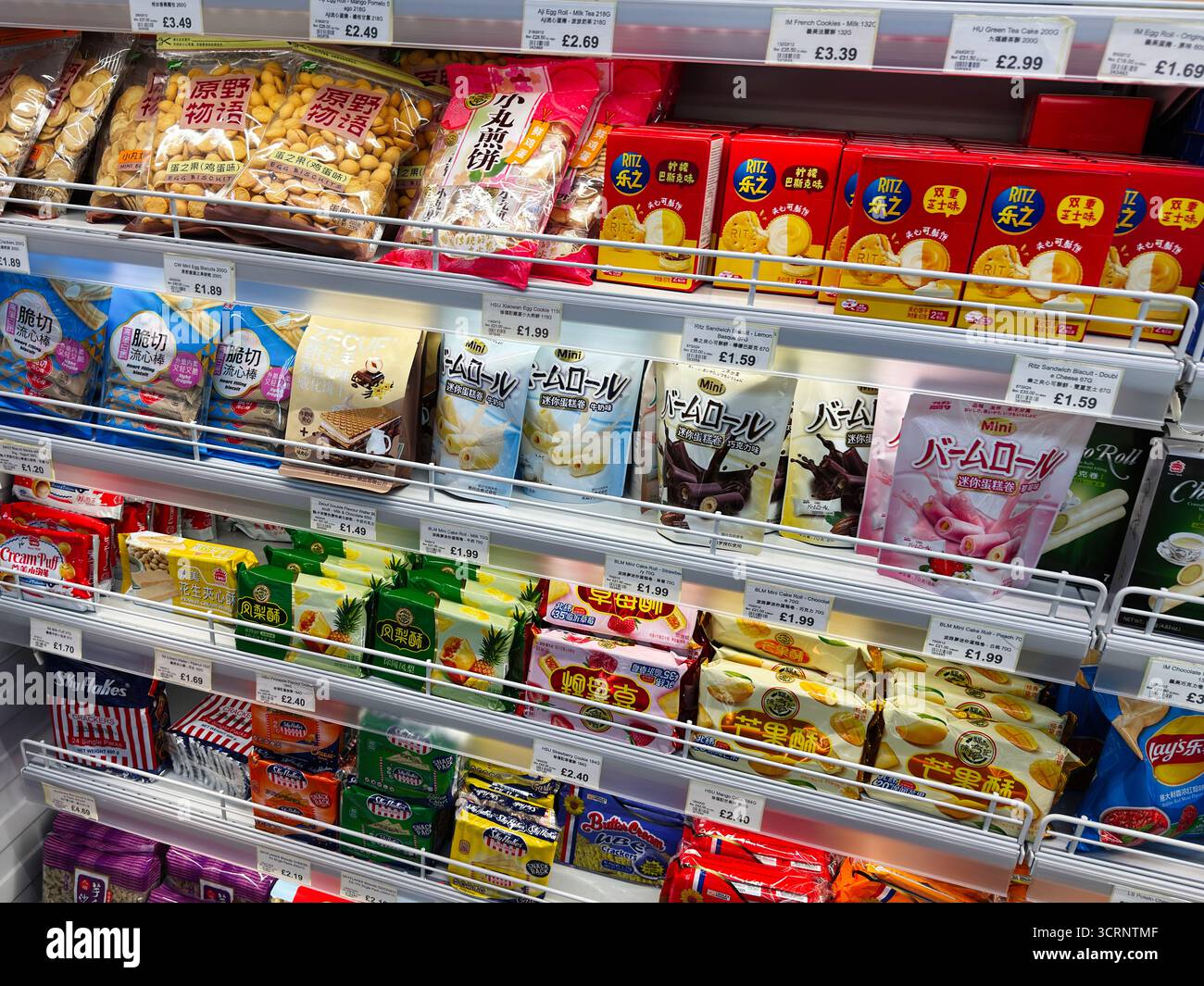 Manchester, Regno Unito - 25 settembre 2025: Pacchetti di snack colorati sugli scaffali dei supermercati in un negozio di alimentari, che mostrano varietà e prezzi. Foto Stock